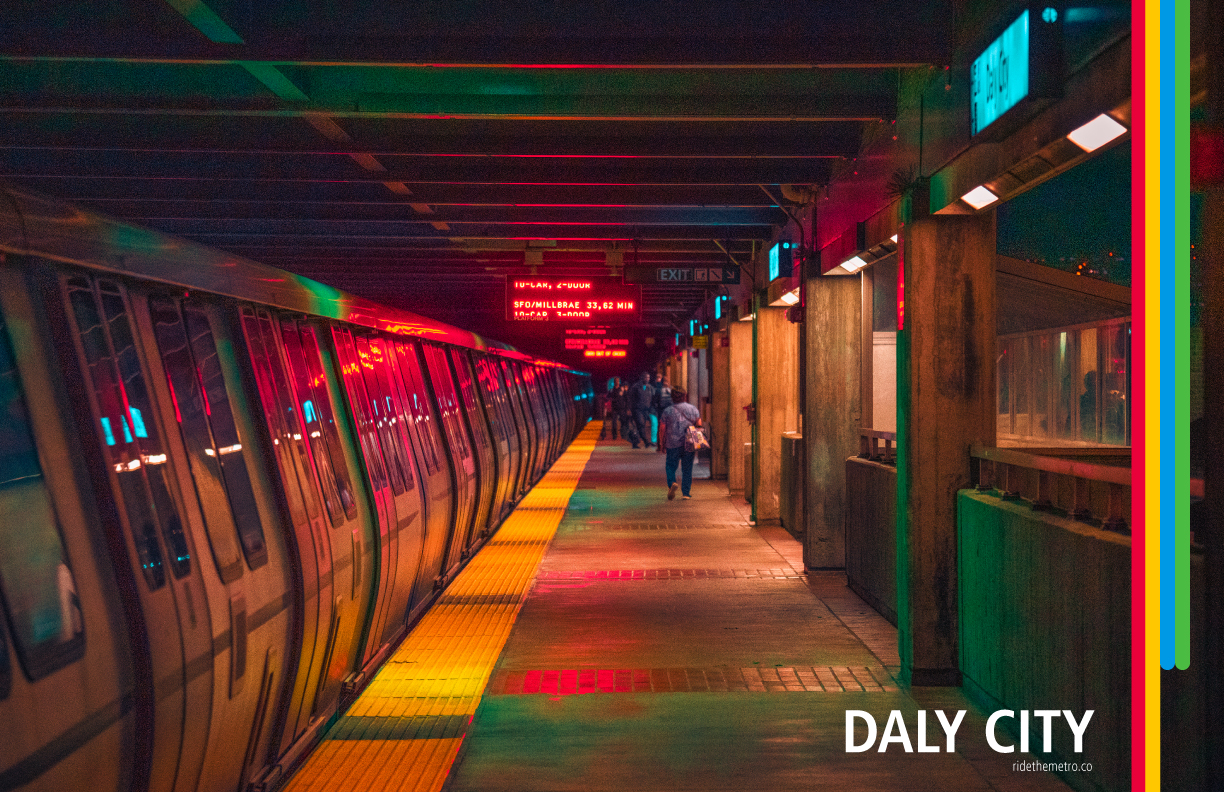 A photo poster that says Daly city, with vertical red yellow blue and green lines overlaid on the right side. The blue and green stripes do not continue all the way across the image. The photo shows the elevated station platform at night with a fleet of the future train pulled in. The platform has a partial roof structure with metal beams going across, and regular concrete columns holding it. There are multiple colours of light in the photo: bright yellow spots on the yellow platform line, red reflections from the overhead signs, and greenish teal lights from unseen overhead lighting. There is a indistinct crowd of people in the distance heading to the platform exit.